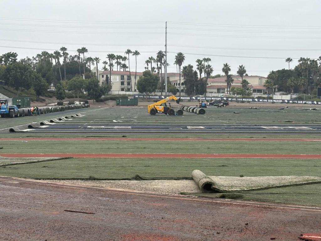 A construction crew works on a sports field, laying down new turf.