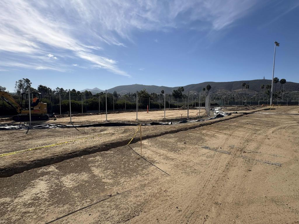 A wide view of an outdoor construction site with cleared dirt ground under a blue sky.