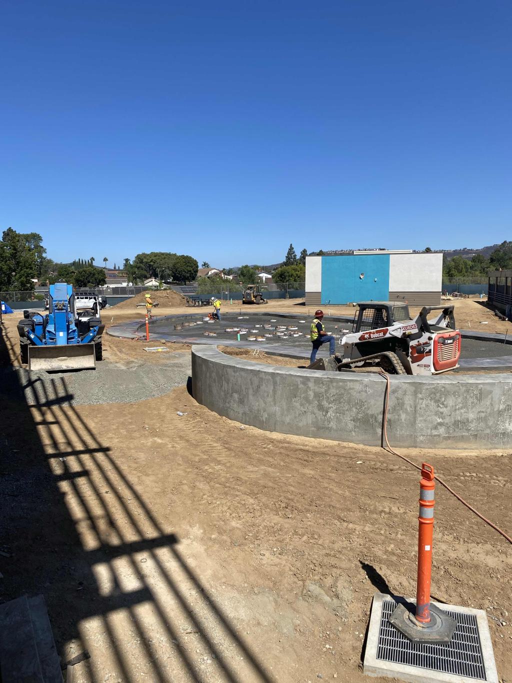 A construction site on a sunny day with heavy machinery, concrete foundations, and clear blue sky.