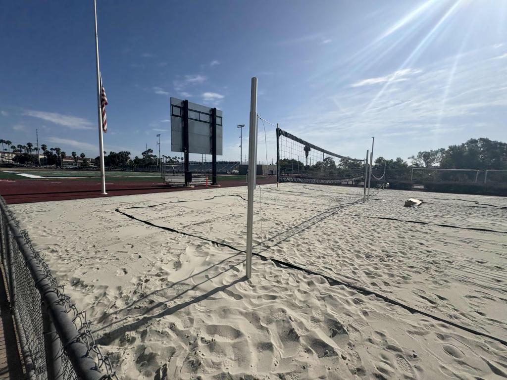 A sunny beach volleyball court stands empty under a clear blue sky.