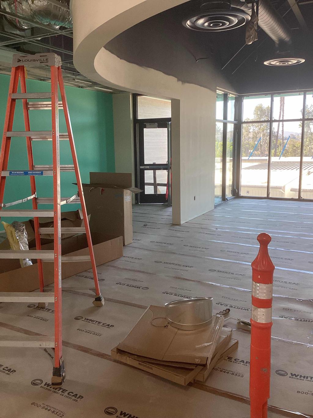 A commercial interior space undergoing renovation, with a tall orange ladder and protective floor covering.