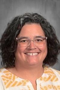 A woman with dark hair and glasses smiling.