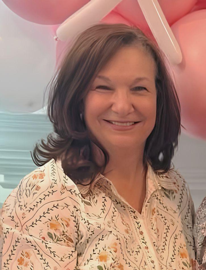 A woman with shoulder-length brown hair smiles warmly, wearing a floral print shirt.