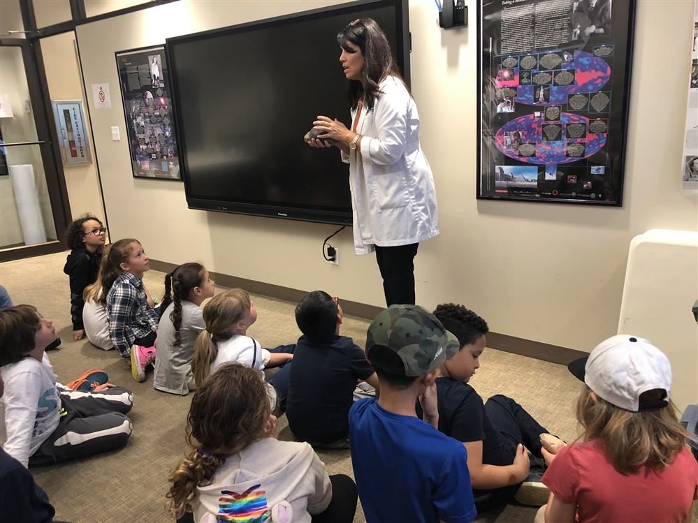 A woman in a lab coat engages with children at the Long Island Science Center.