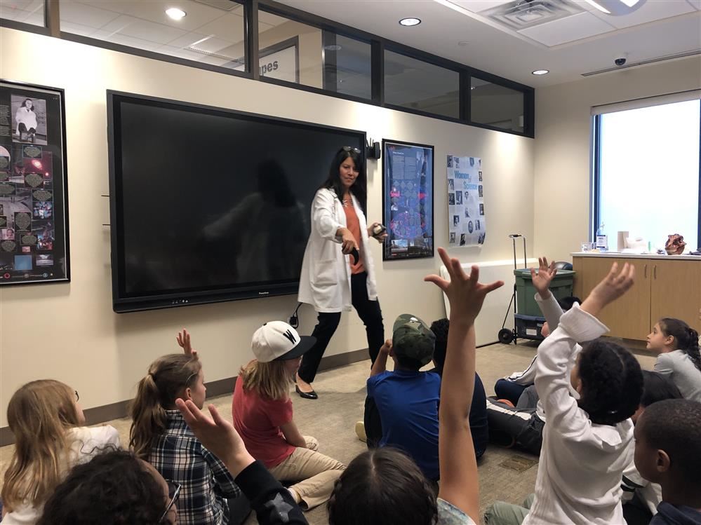 A woman in a lab coat teaches children about science at Long Island Science Center.