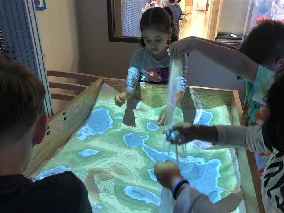 Children playing with an interactive map on a table at the Long Island Science Center.
