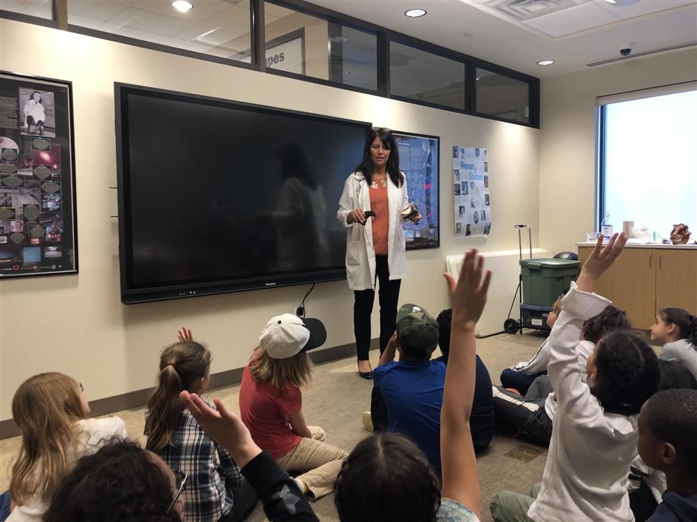 A woman in a lab coat teaches children about science at the Long Island Science Center.