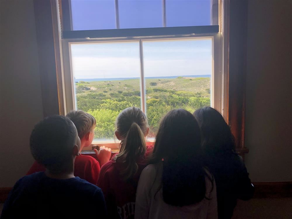 Four children gaze out window at ocean.