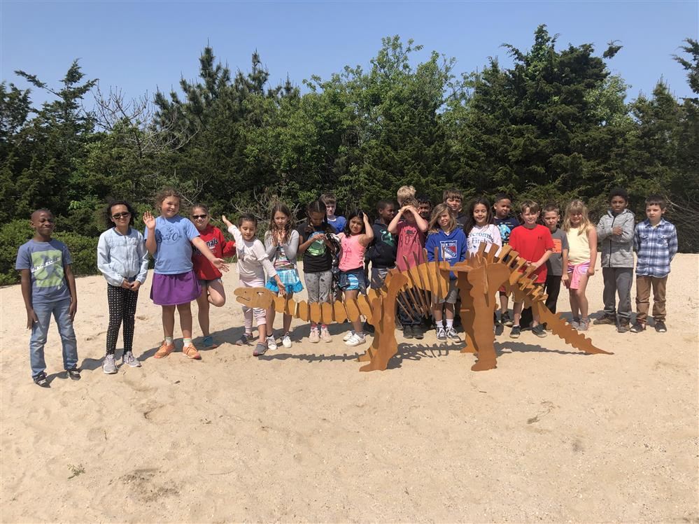 A group of kids posing with a wooden dinosaur sculpture at the Dinosaur Dig/Lifesaving Station.