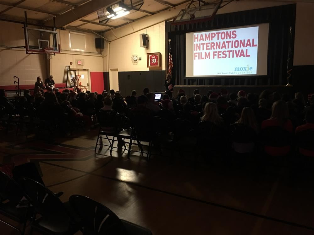 A diverse crowd of people sitting in chairs in a gymnasium, engaged in an event or gathering.