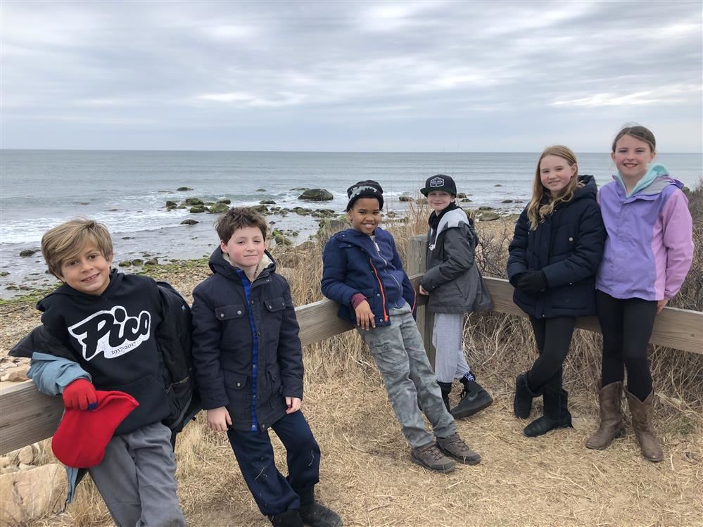 A group of kids standing on a wooden boardwalk near the ocean, enjoying the scenic view and the fresh sea breeze.
