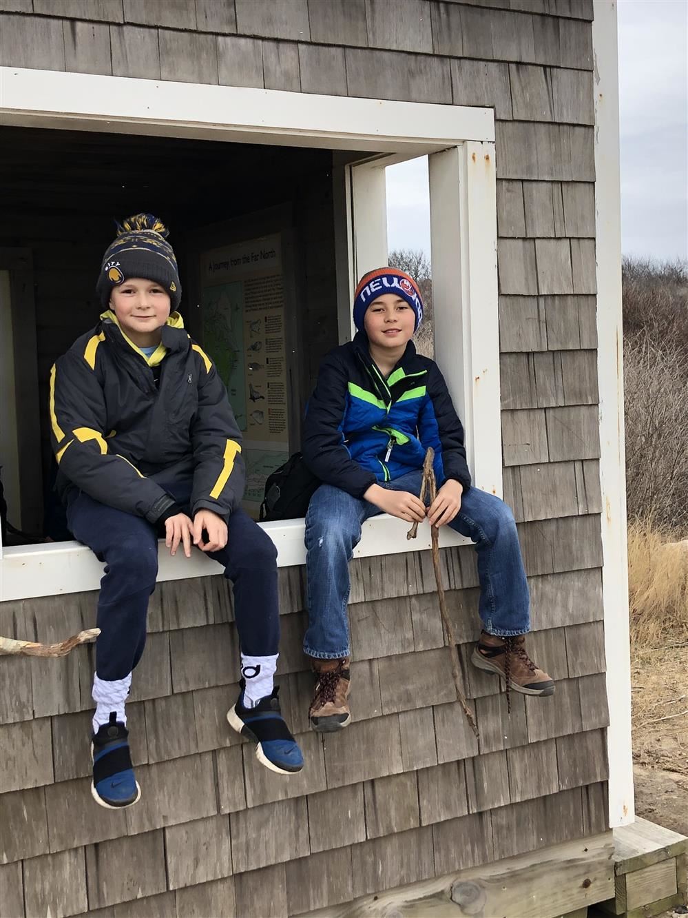 Two boys sitting on the edge of a wooden house, enjoying each other's company.