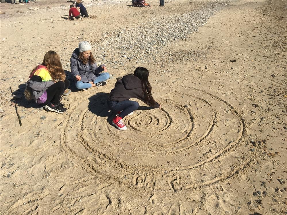 Three children drawing a spiral on the sand