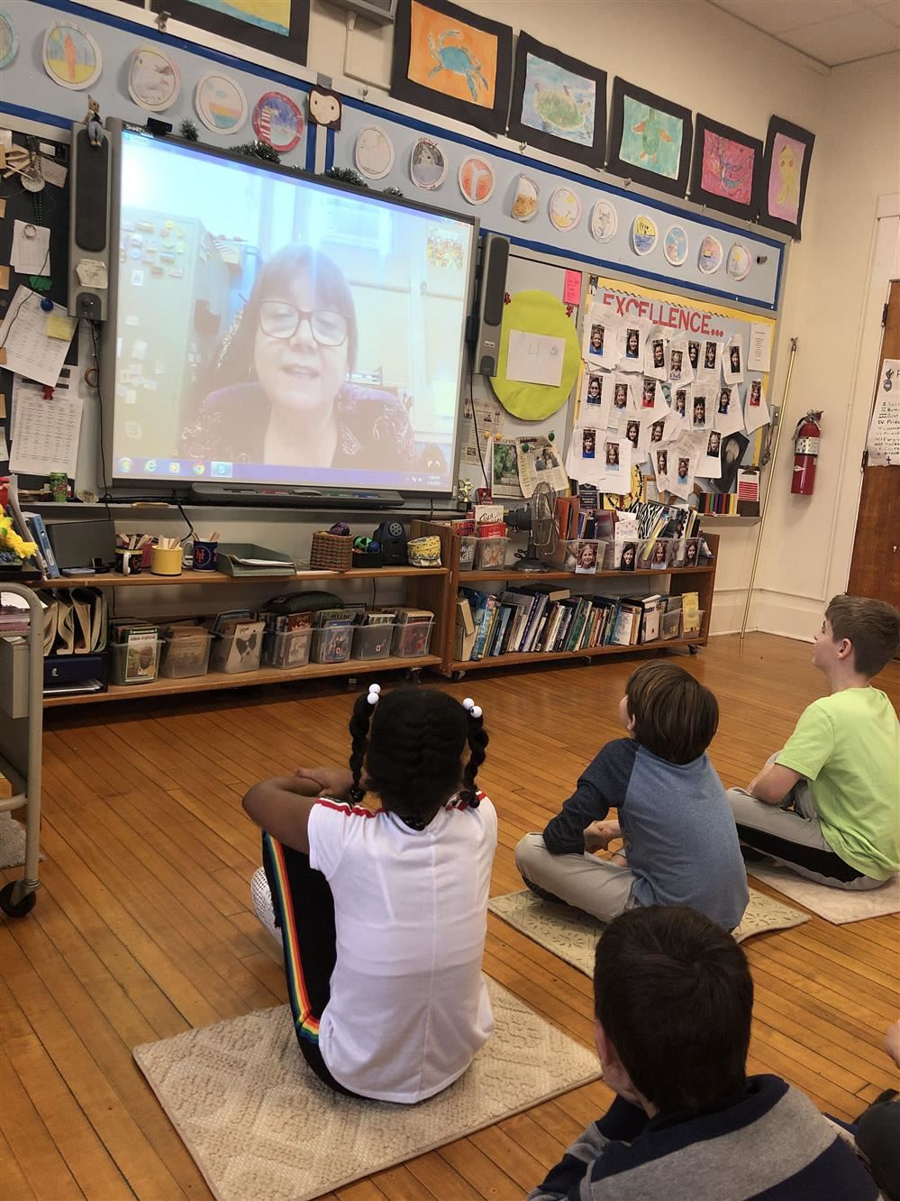 A group of children sitting on the floor, engrossed in watching a video on a screen.
