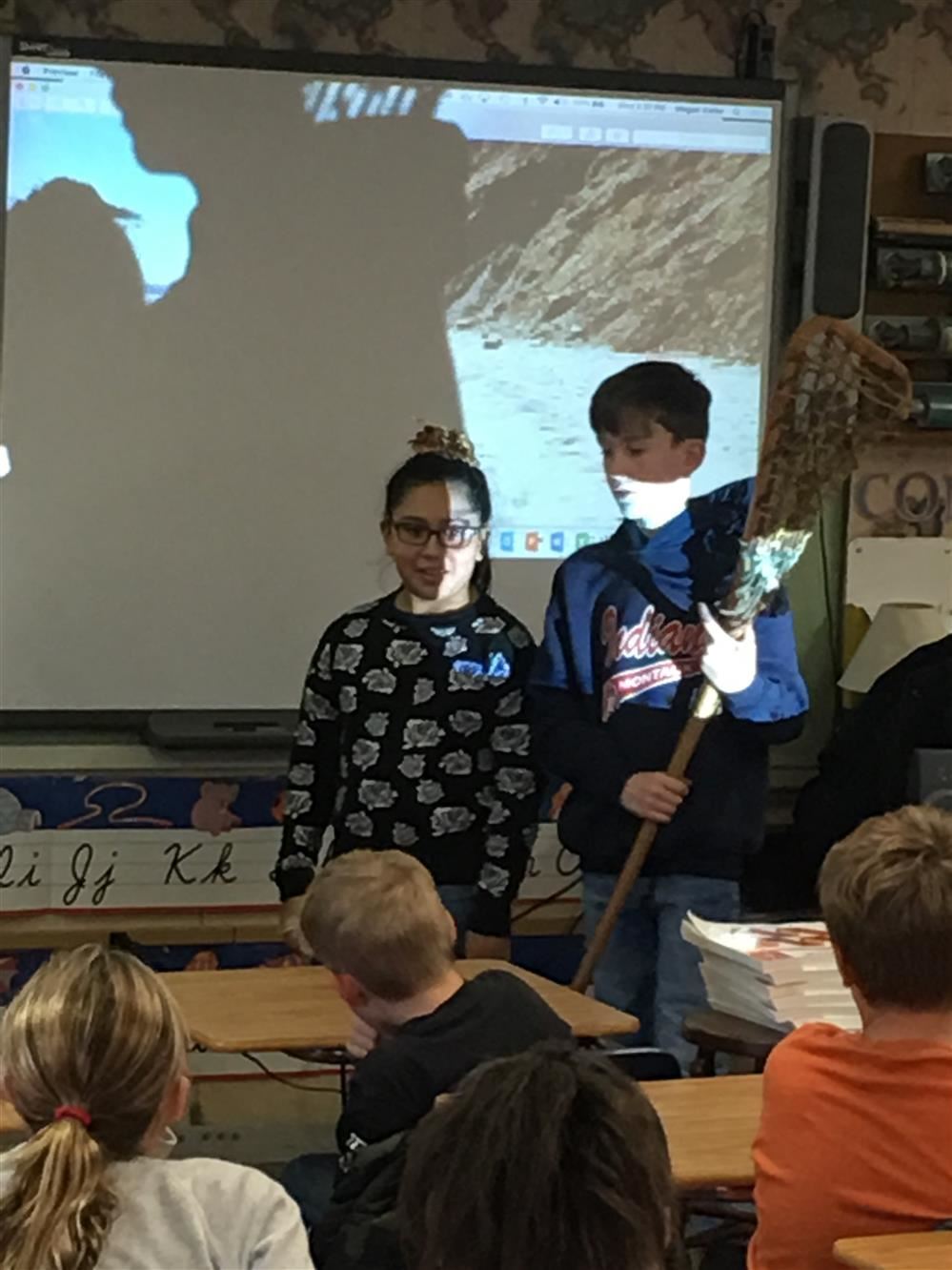Two children standing in front of a classroom with a projector screen.