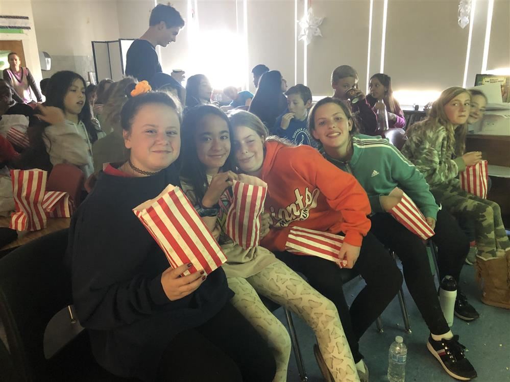 A group of girls sitting in chairs, enjoying popcorn together.