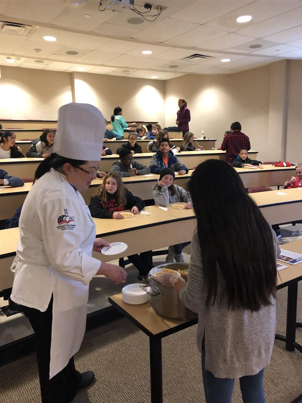 A chef serving food to students in a classroom.