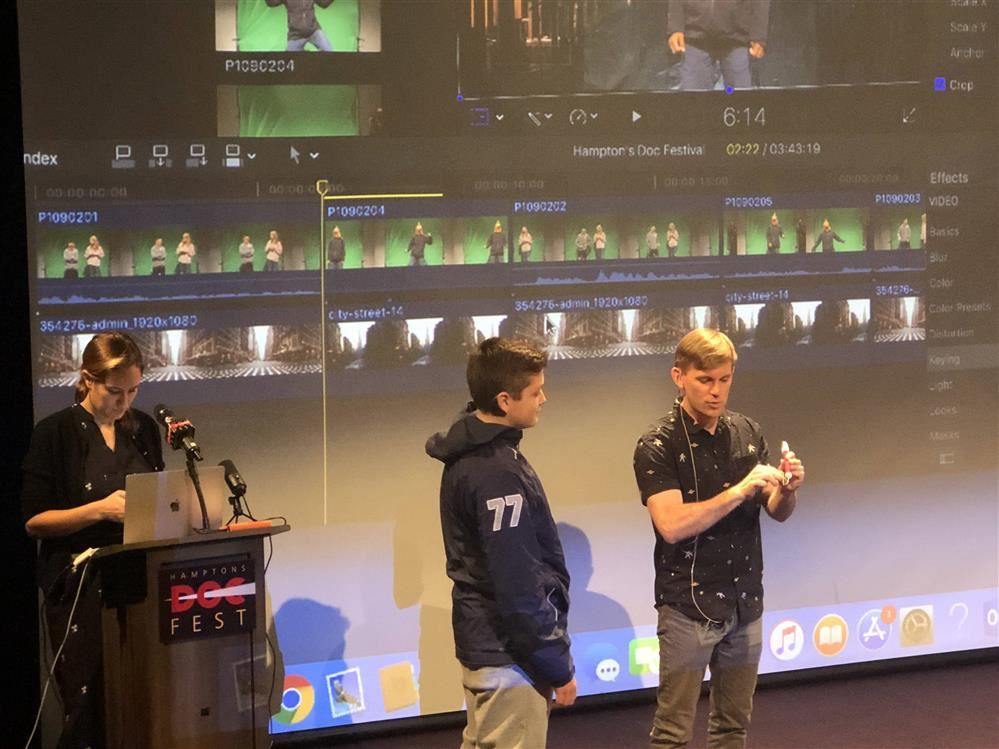 Two individuals standing in front of a screen, illuminated by a projector's light.