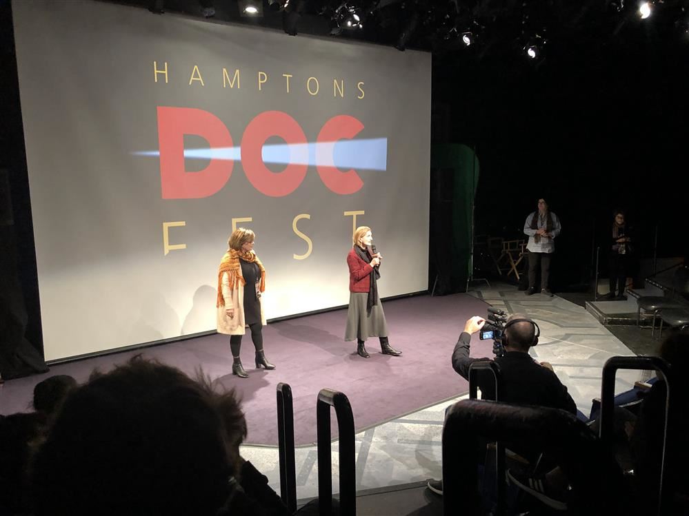 Two women on stage at the Hamptons Doc Fest, engaging with the audience during a captivating presentation.