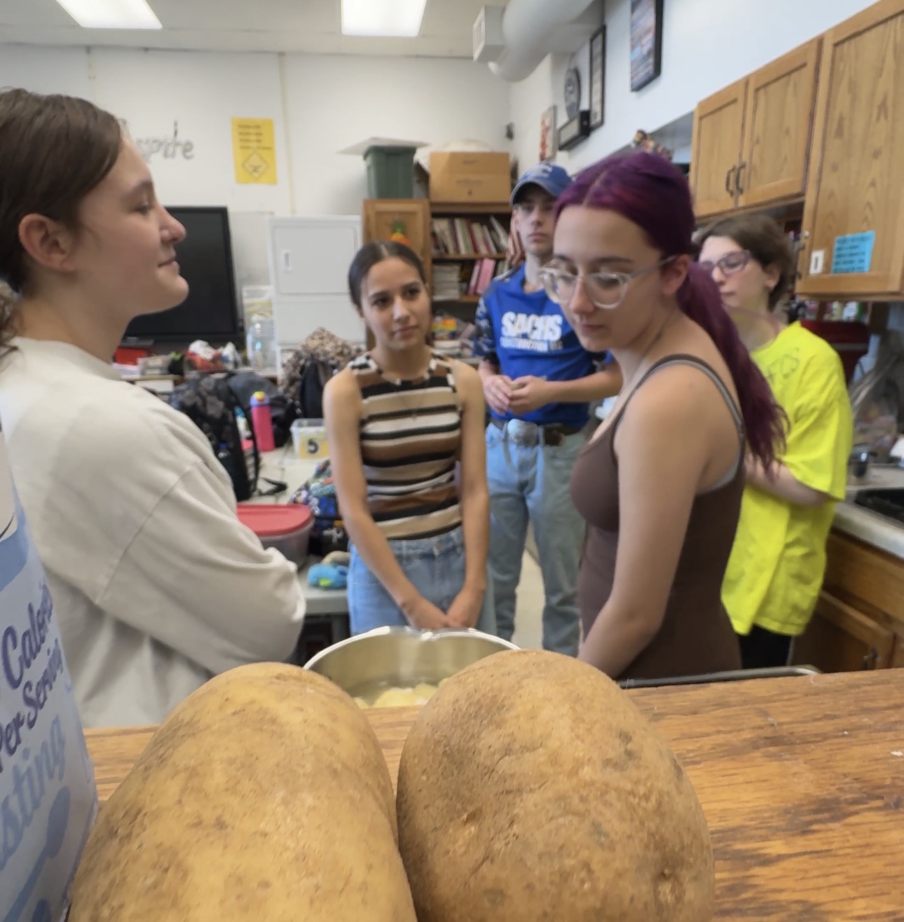 five students standing around stovetop making mashed potatoes