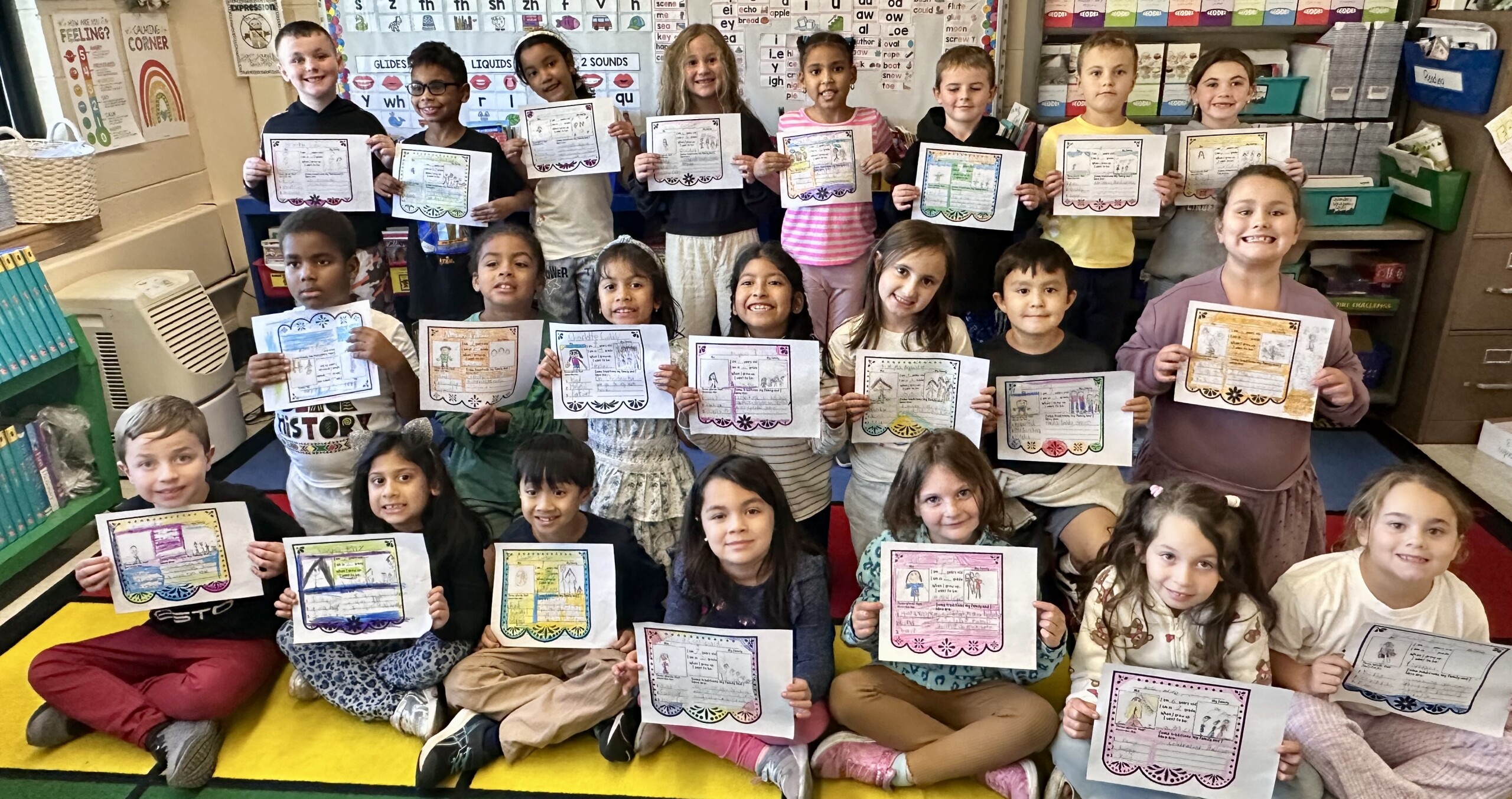 A teacher and a large group of elementary students proudly hold up their certificates in a brightly decorated classroom.