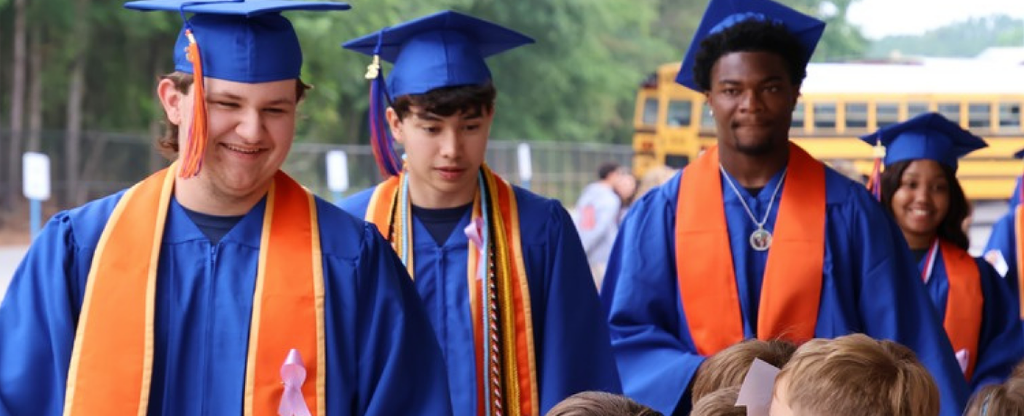 A group of students in blue graduation caps and gowns walk outdoors.