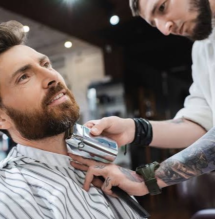 A barber carefully trims a customer's beard with clippers in a modern salon.