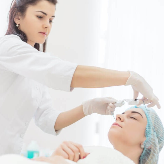 A professional practitioner in a white uniform prepares a client for a cosmetic procedure in a bright, clean clinic.