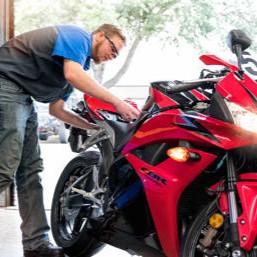 A mechanic in a blue shirt works on a vibrant red motorcycle inside a garage.
