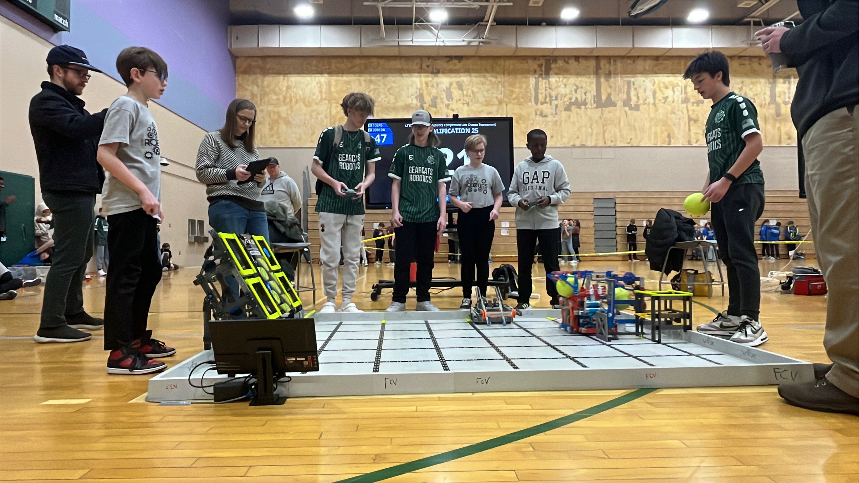 Students and adults participate in a robotics competition in a gymnasium.