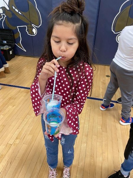 A young girl holds two cups with straws.