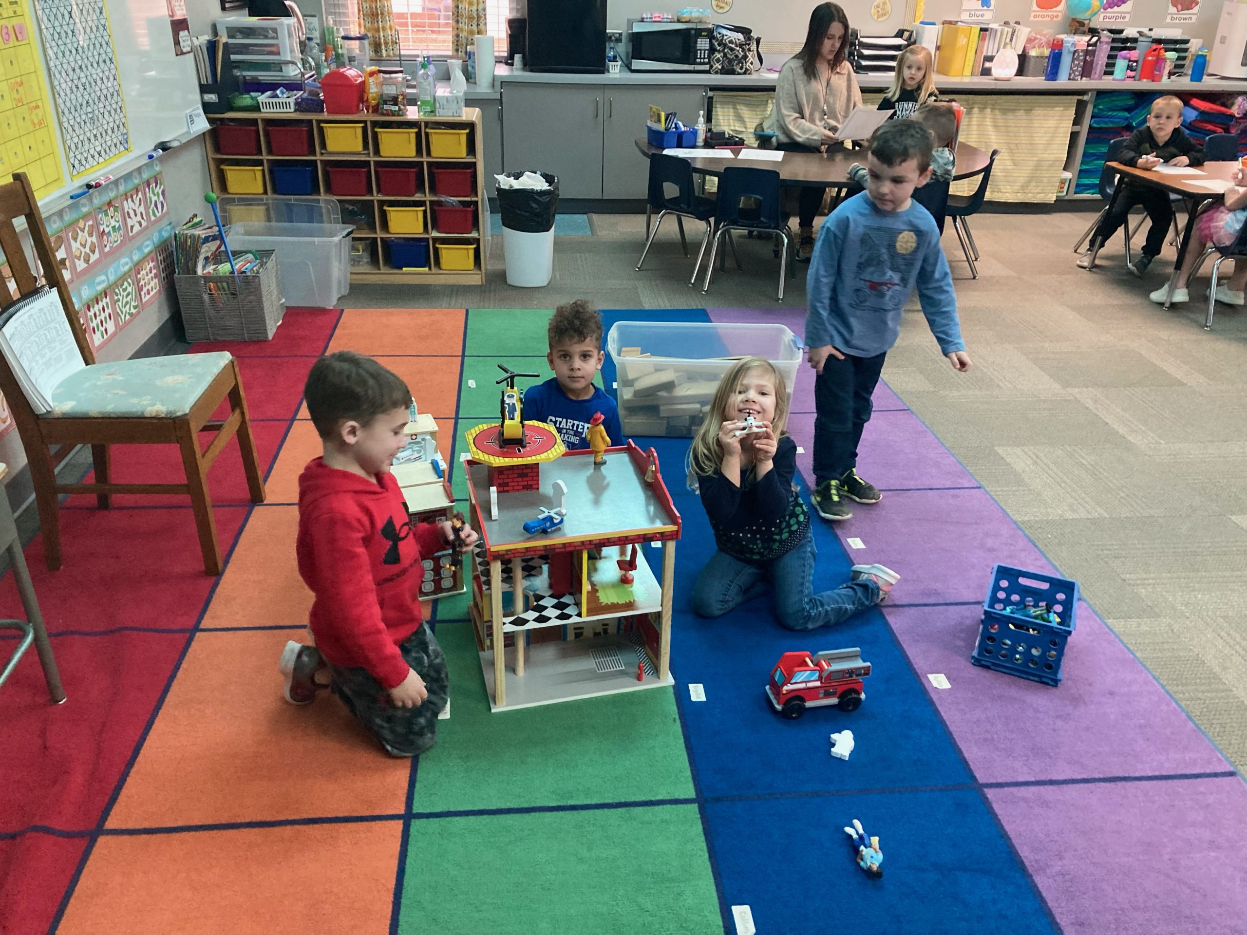 A group of children are playing with toys on the floor in a classroom.
