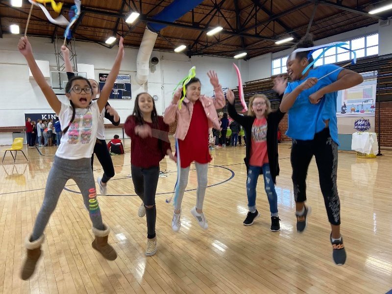 A group of children are jumping in the air while holding ribbons.