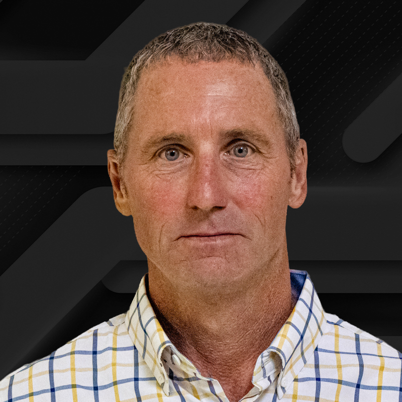 Close-up portrait of a middle-aged man with short, graying hair, wearing a checkered shirt.