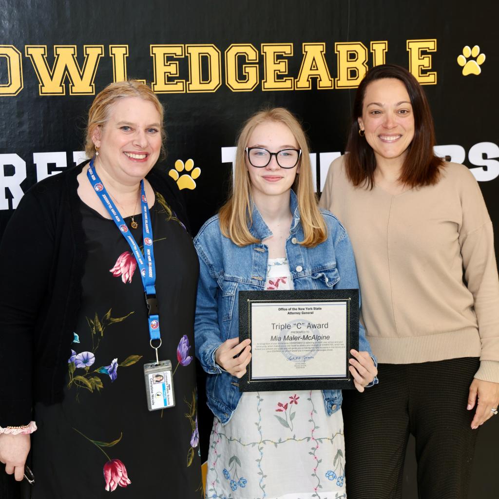 A young person holds an award, flanked by two smiling adults.