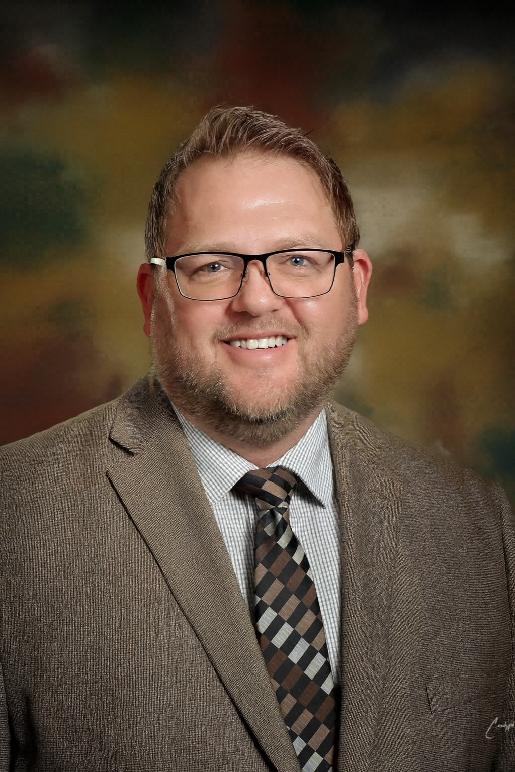 A man with glasses smiles, wearing a suit and tie.
