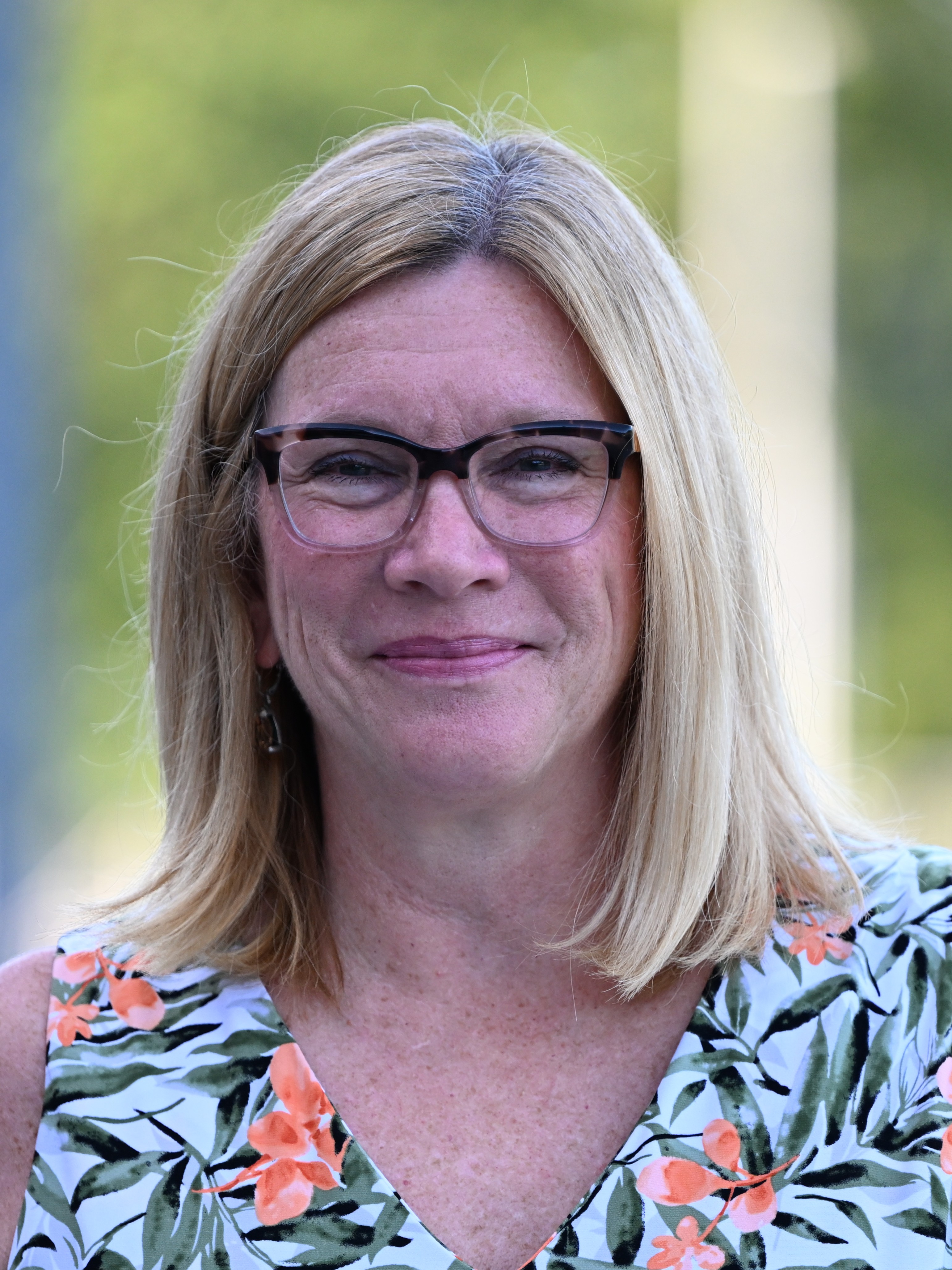 A woman with blonde hair and glasses smiles at the camera.