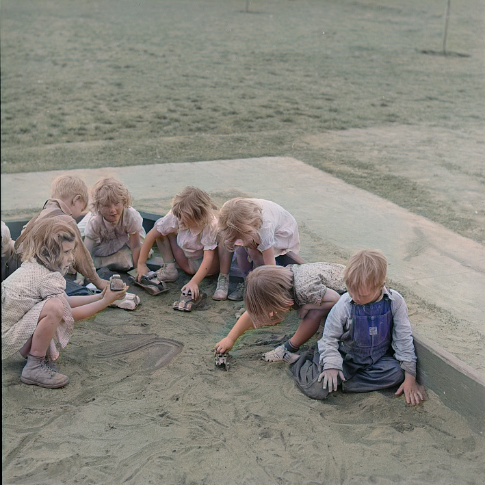 A group of children play in a sandbox, creating patterns in the sand.