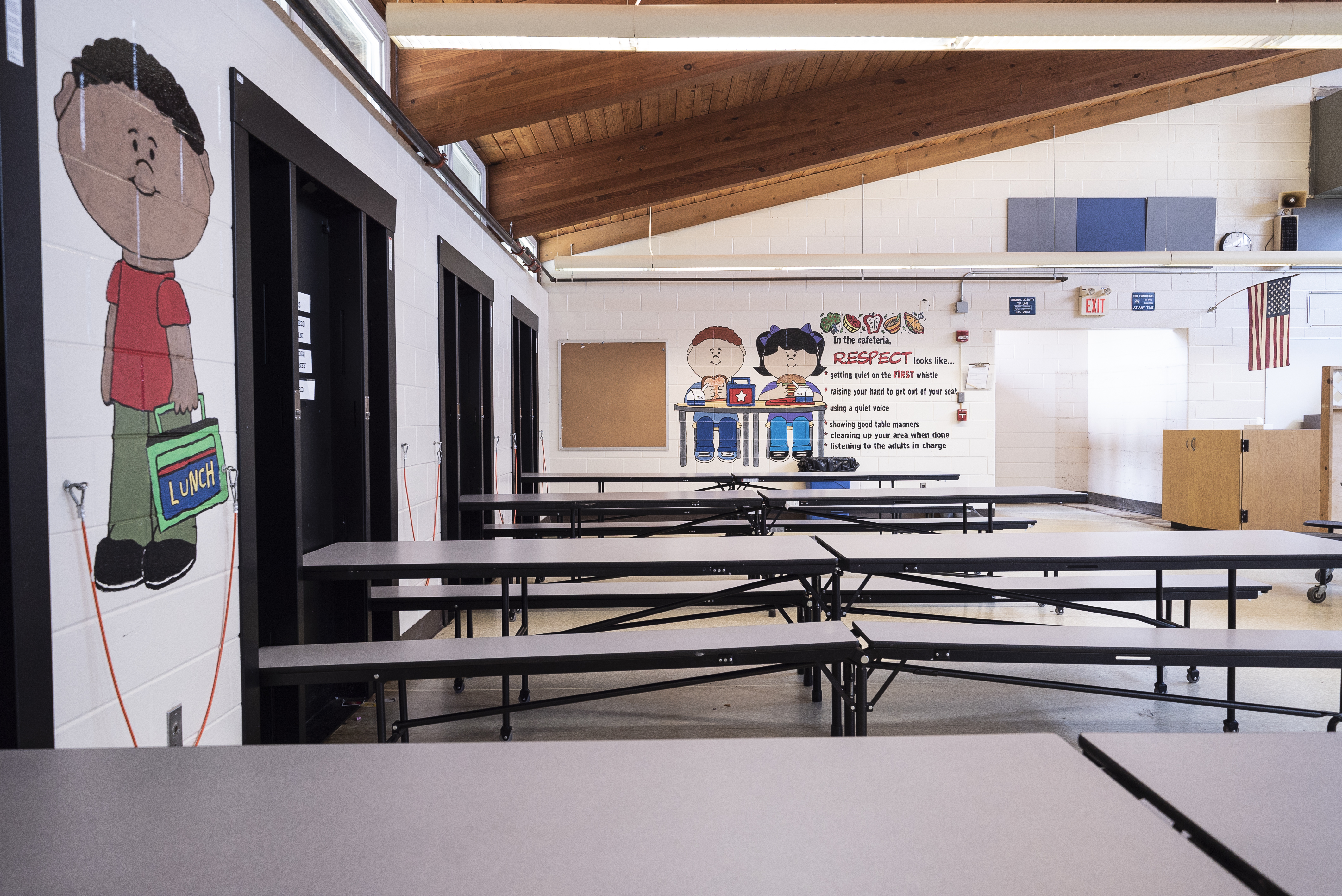 An empty school cafeteria with rows of tables and benches, decorated with student artwork.