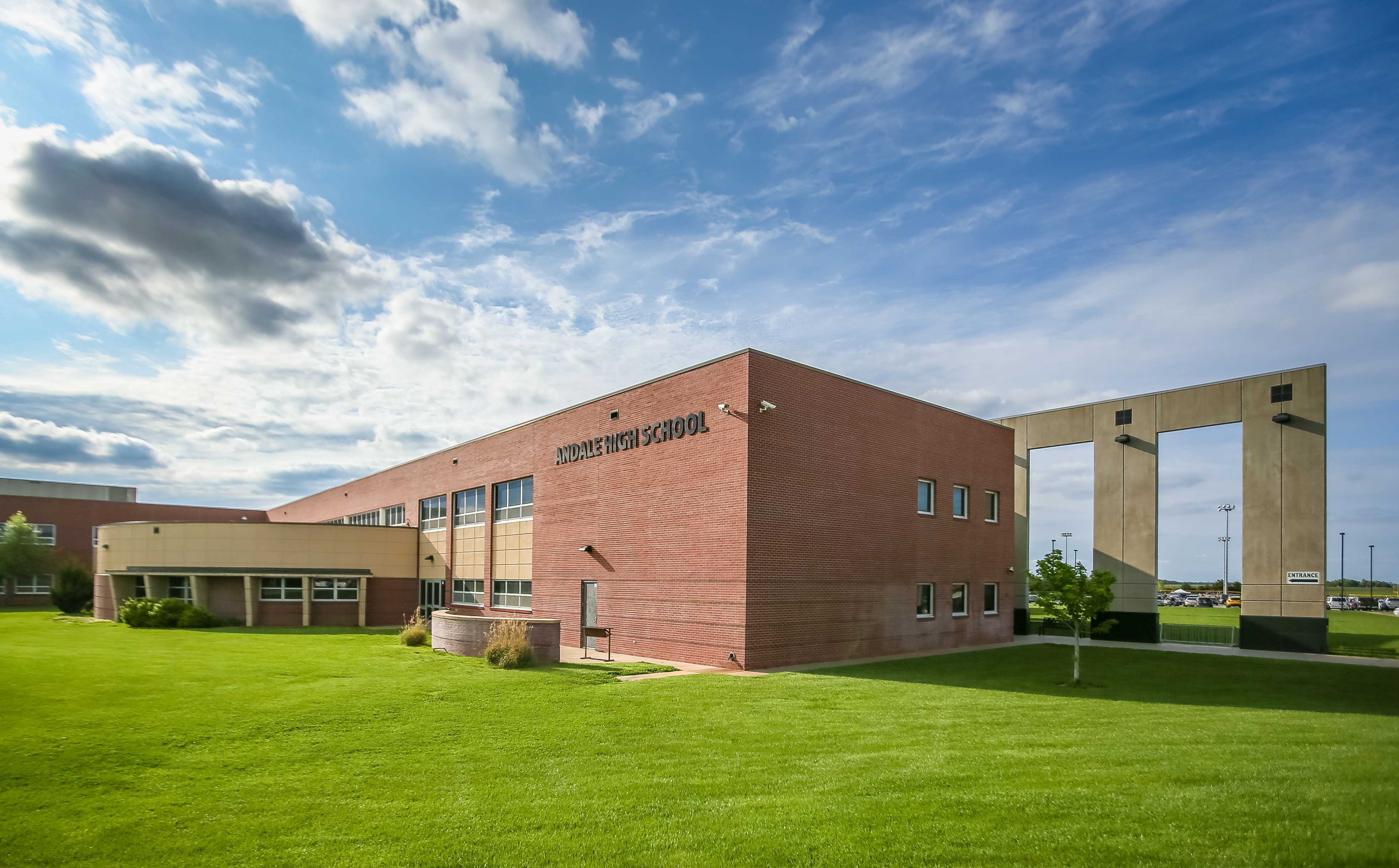 A modern brick building with large windows sits on a green lawn under a blue sky.