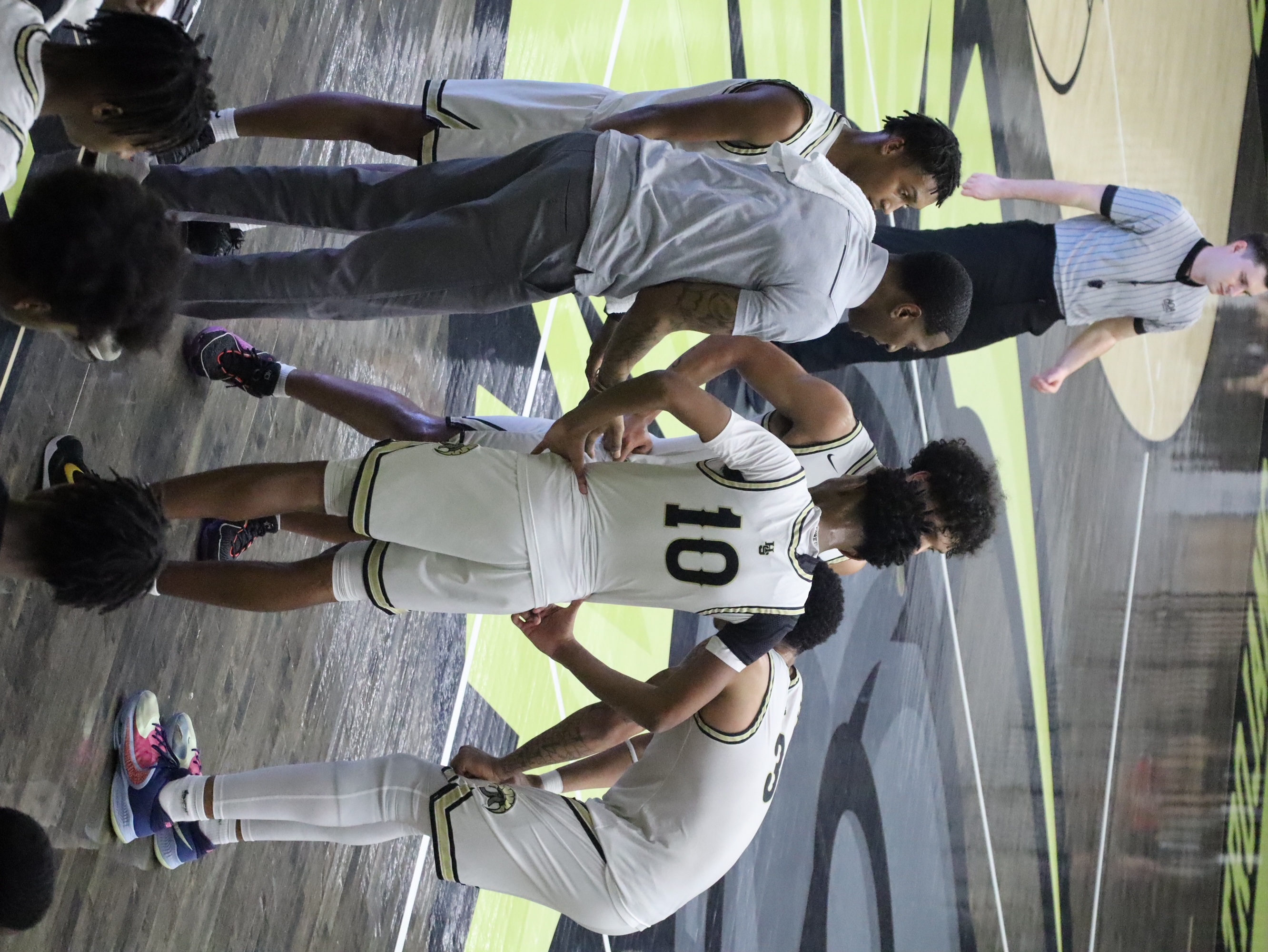 Basketball players huddle together on the court, listening to their coach.