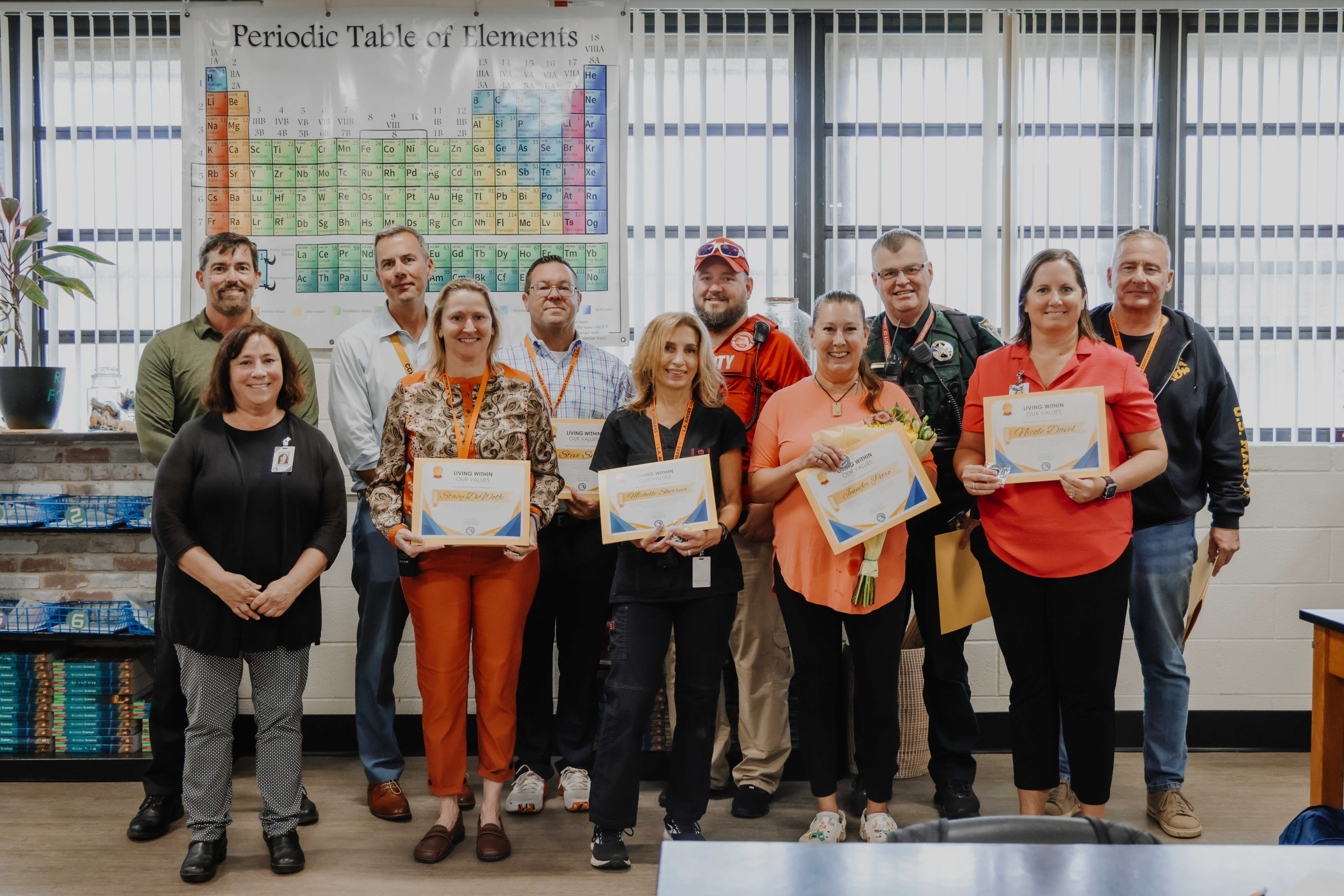 A group of people stand together, holding certificates, in a well-lit room.