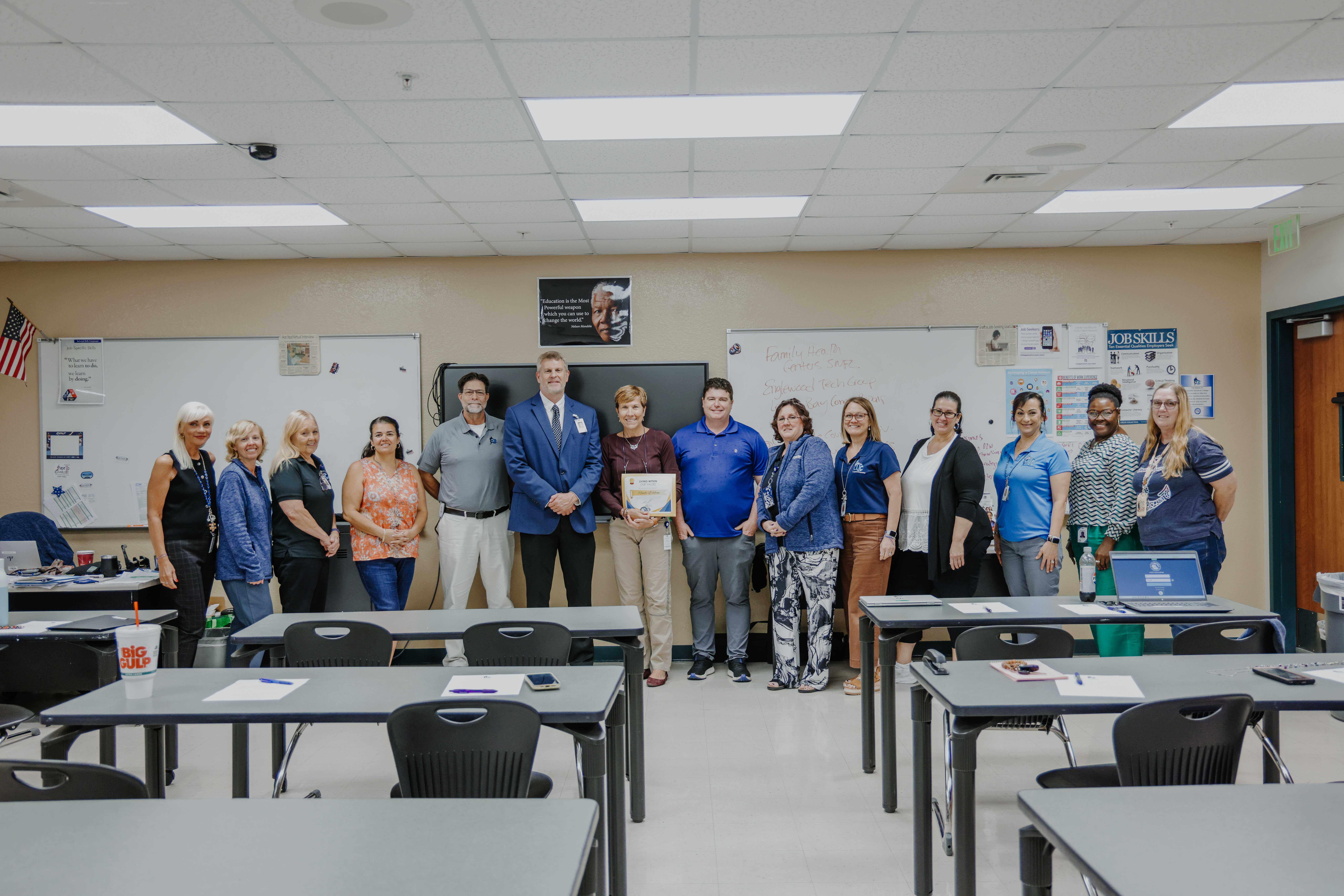 A group of people stand together in a classroom, smiling at the camera.