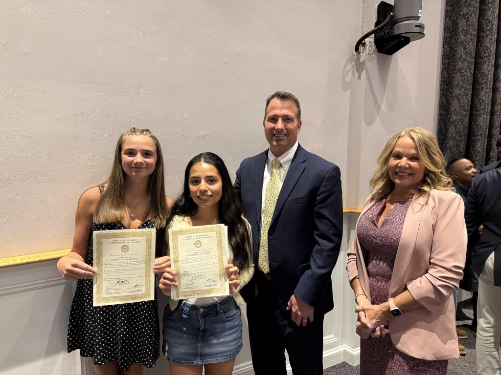 Two young women proudly hold certificates of recognition, standing with two adults.