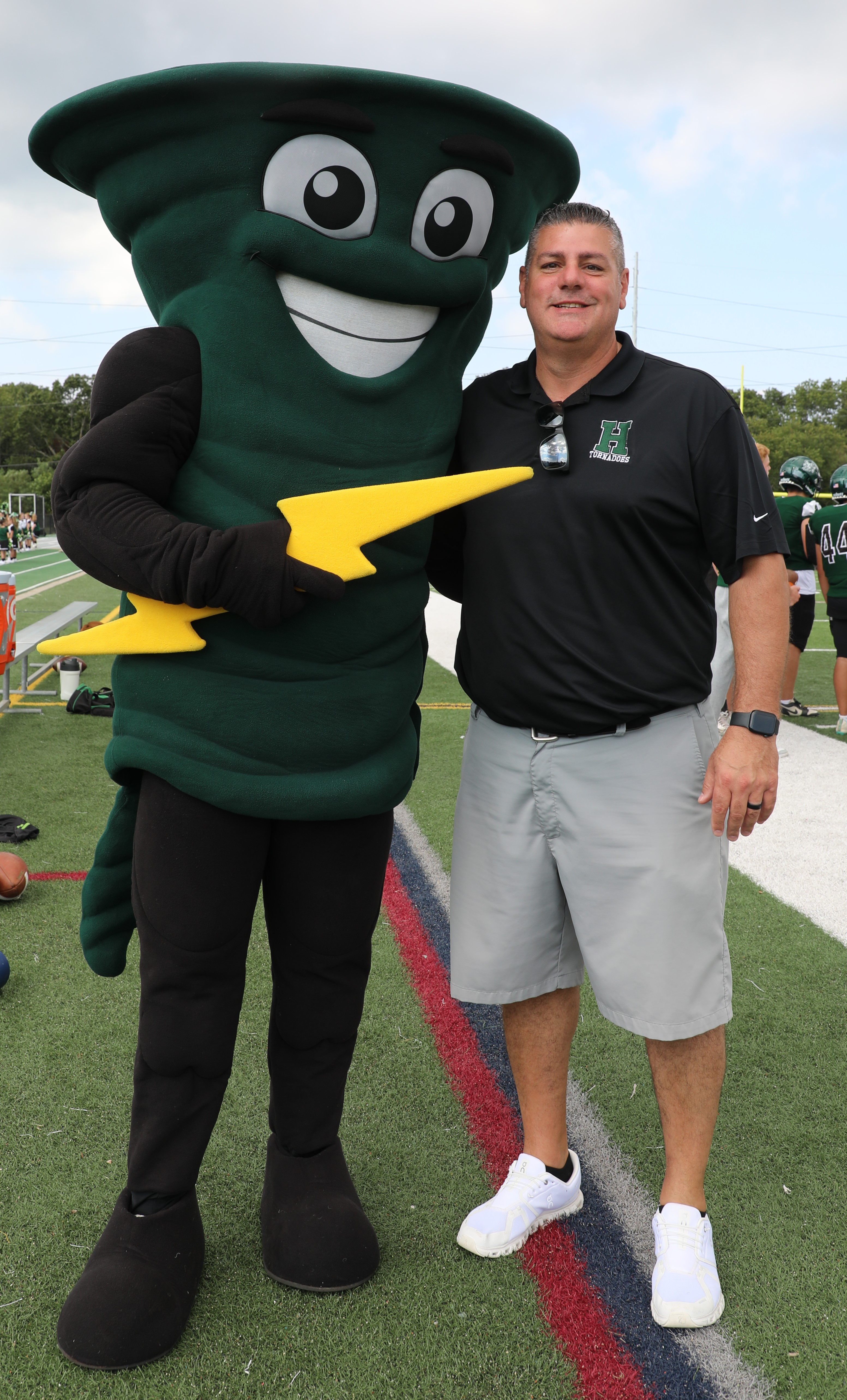 A man poses with a school mascot, a green tornado holding a yellow lightning bolt.