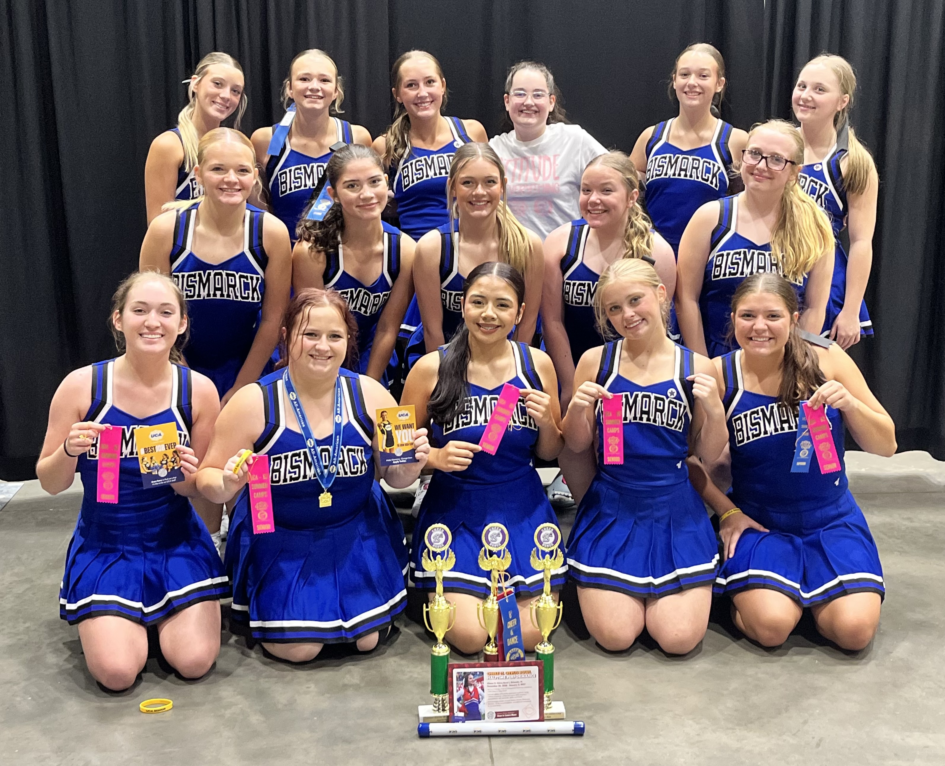 A cheerleading team poses for a photo with trophies and ribbons.