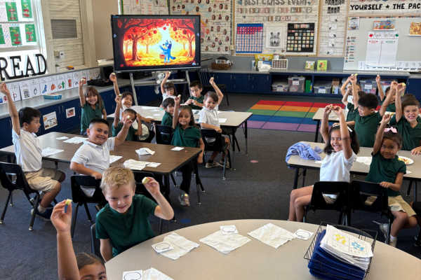A bright elementary classroom where eager young students sit at desks and raise their hands.