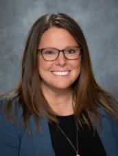 A woman with long brown hair and glasses smiles at the camera.
