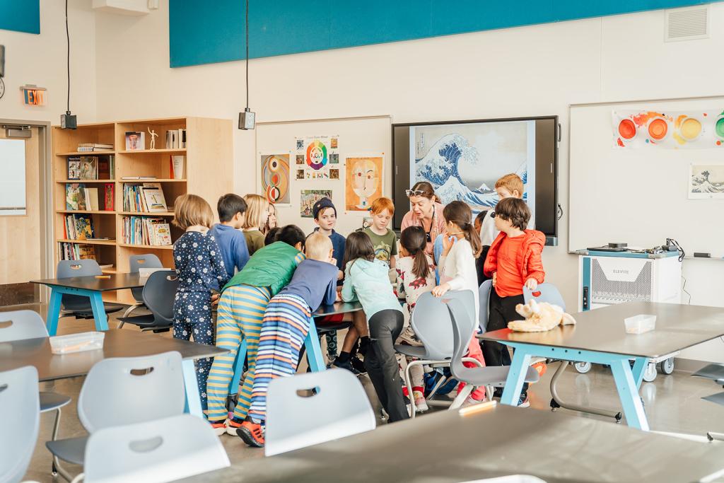 A group of children gather around a table in a brightly lit classroom.