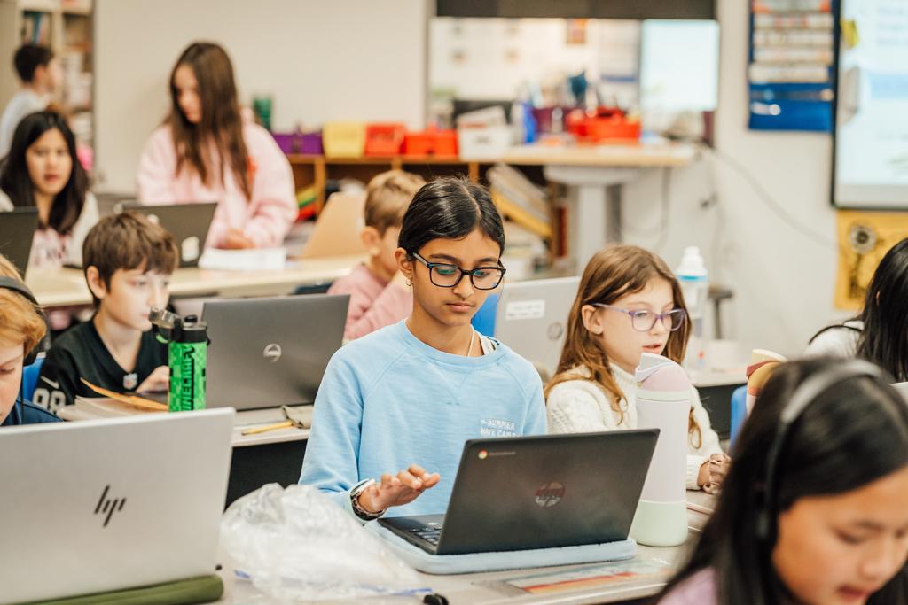 Students focus on their laptops in a bright classroom setting.